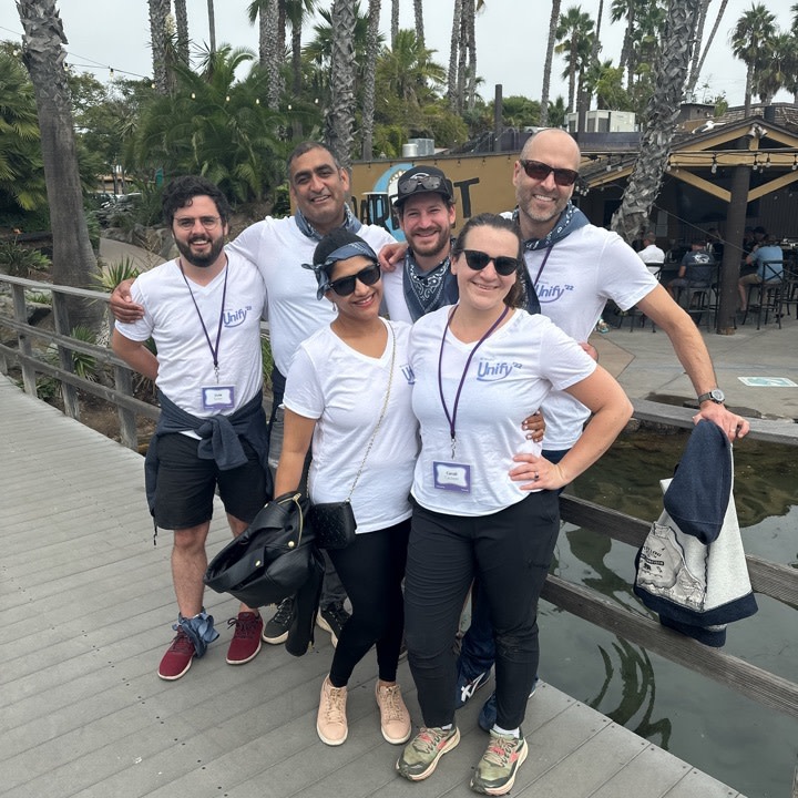 Five colleagues wear matching Vendia t-shirts at the company retreat with palm trees in the background